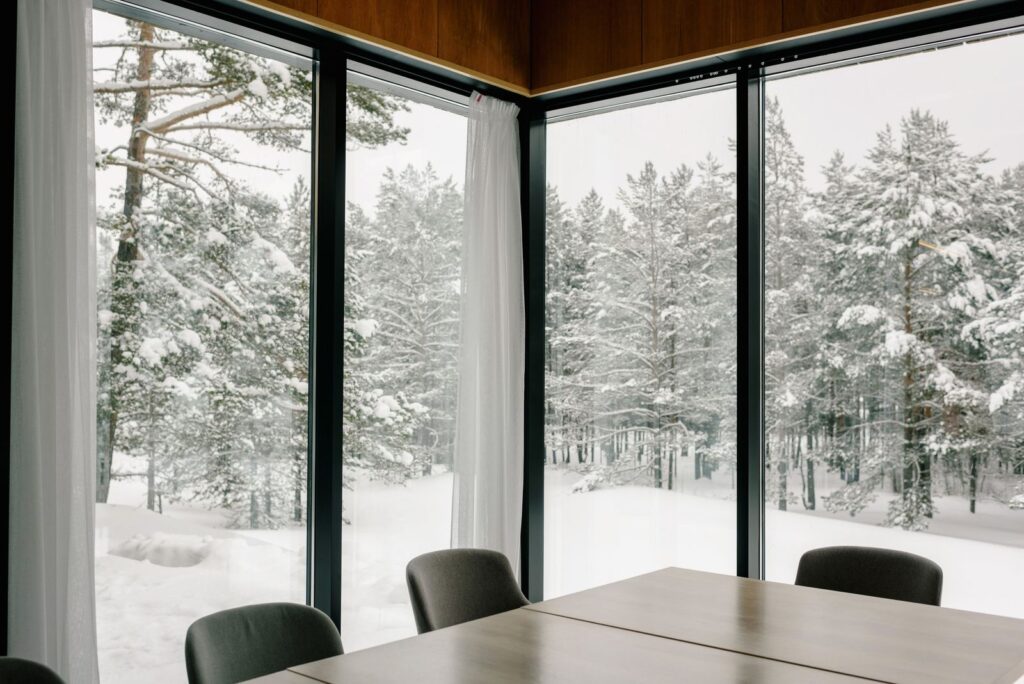 Large lakehouse windows looking out on a snow-covered Northwoods forest